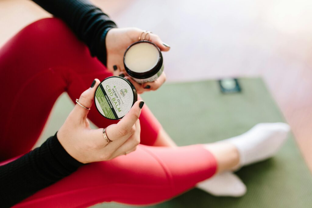 Close-up of a woman holding CBD balm while seated on a yoga mat, showcasing top CBD benefits.
