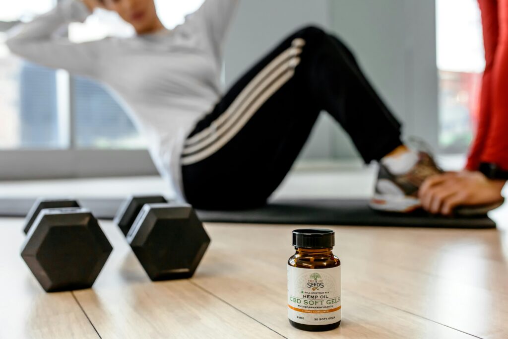 Focused image of CBD soft gels bottle on gym floor with person exercising in the background.