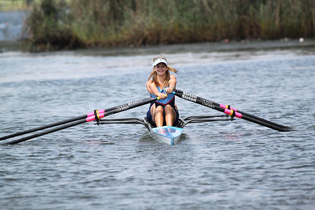 Smiling woman rowing a scull on a calm lake, enjoying outdoor water sports, Sports for Cardiovascular Health