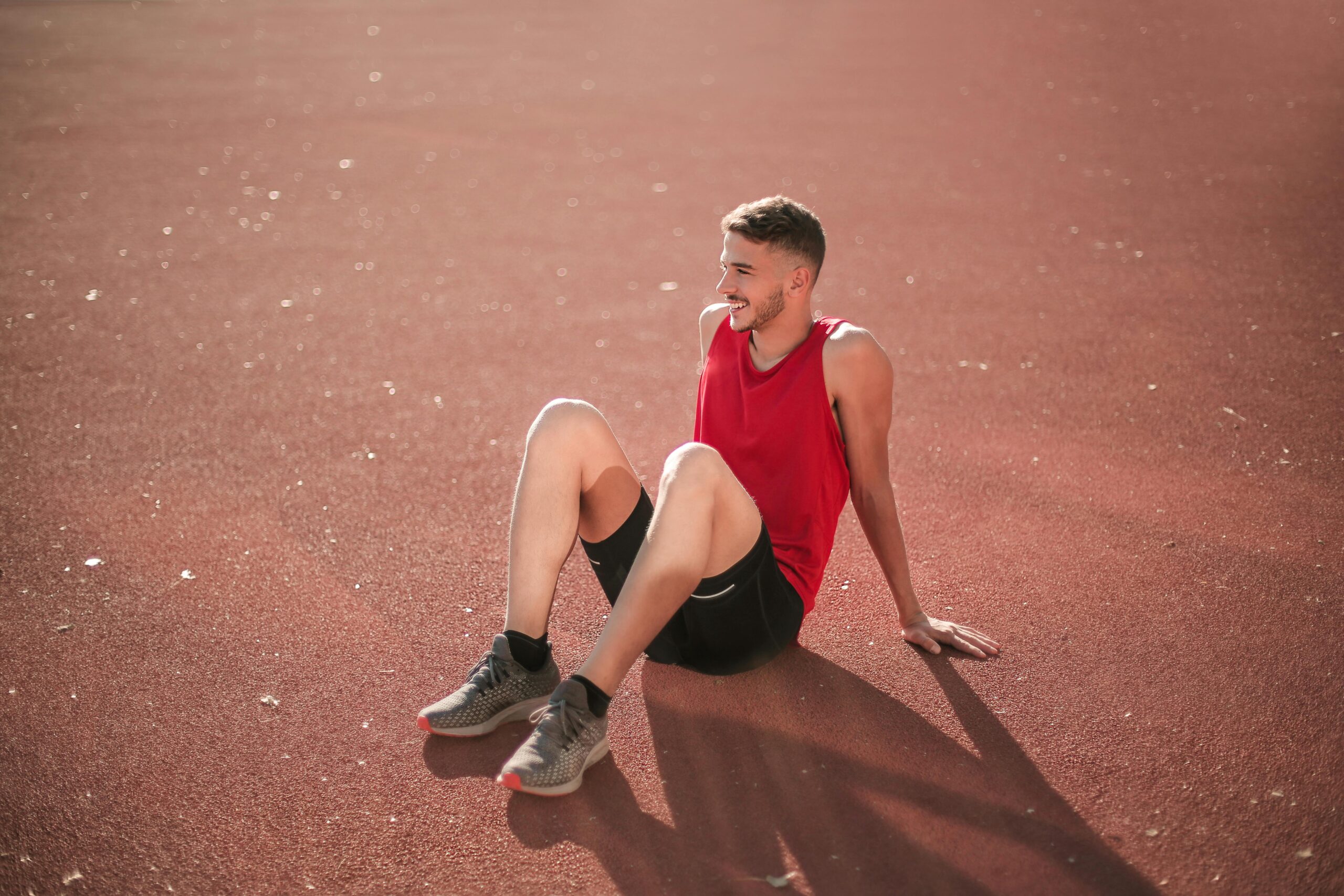 A young man in sportswear relaxing on an outdoor track field in daylight.