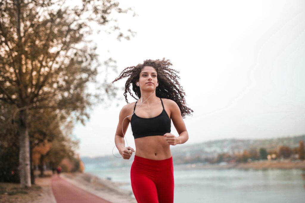 Determined woman in red leggings jogging along a scenic riverside path, embracing fitness outdoors.