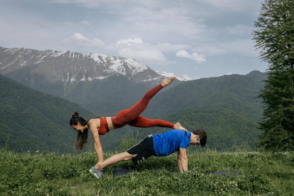 Couple doing yoga exercises outdoors with a breathtaking mountain view.