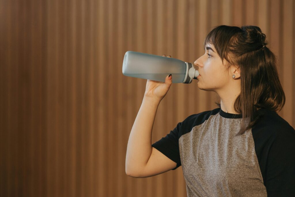 Side view of a woman drinking water from a bottle, promoting healthy lifestyle and fitness.