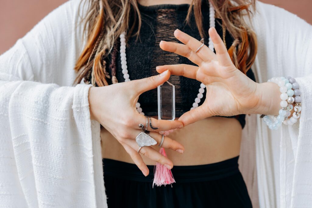 A woman wearing jewelry holds a clear healing crystal, symbolizing spiritual wellness.