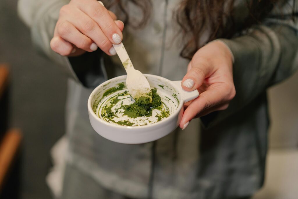 Close-up of a woman preparing a green paste in a ceramic bowl, focusing on hands and texture, foods support mental focus