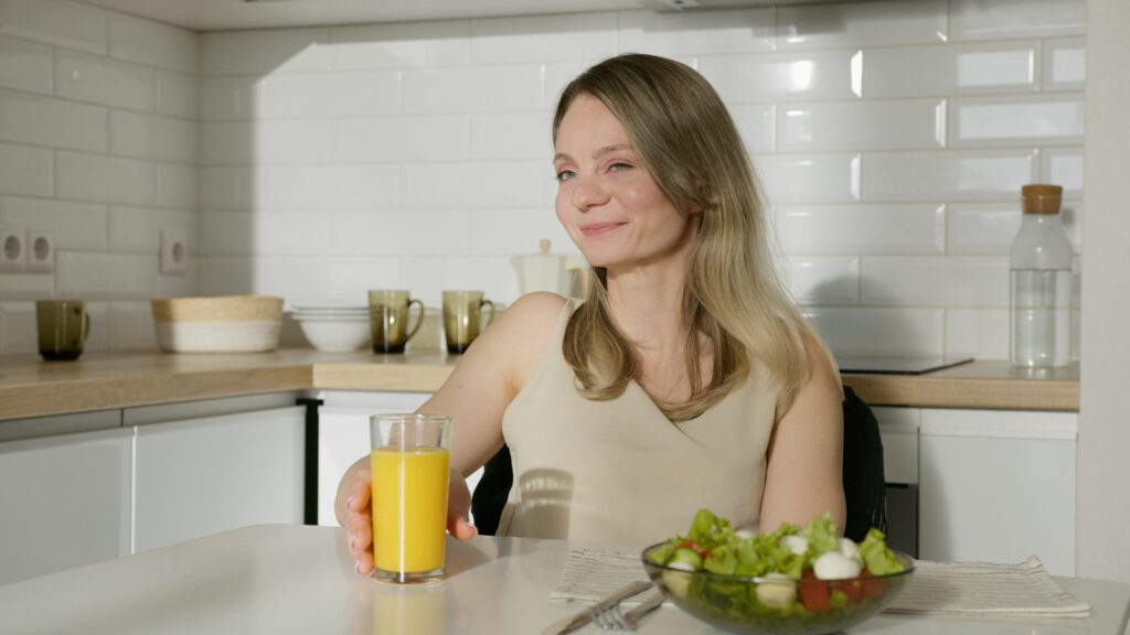 Smiling woman enjoying a healthy meal with salad and orange juice in a modern kitchen and improving gut health.