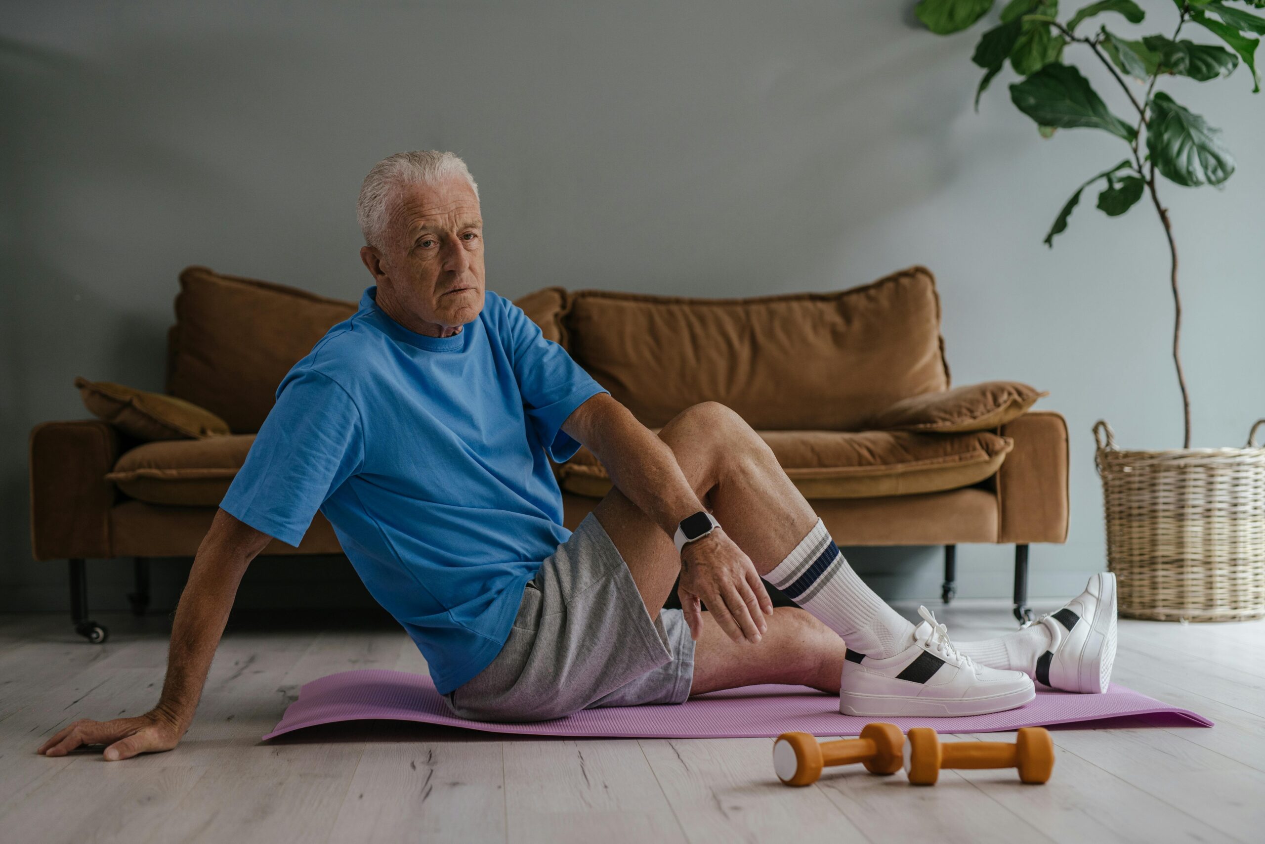 Elderly man enjoys a healthy lifestyle by exercising indoors on a yoga mat with weights.