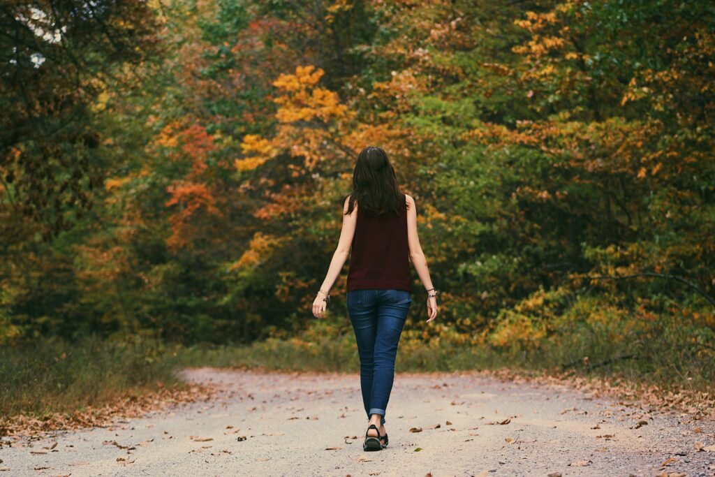 A young woman walks down a colorful autumn forest path, surrounded by vibrant leaves and making daily walking habit.
