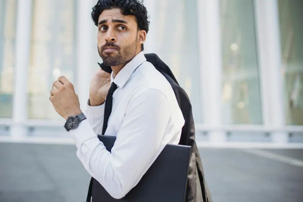 A confident man in corporate attire holding his jacket casually over his shoulder in an urban setting and walking during their work.