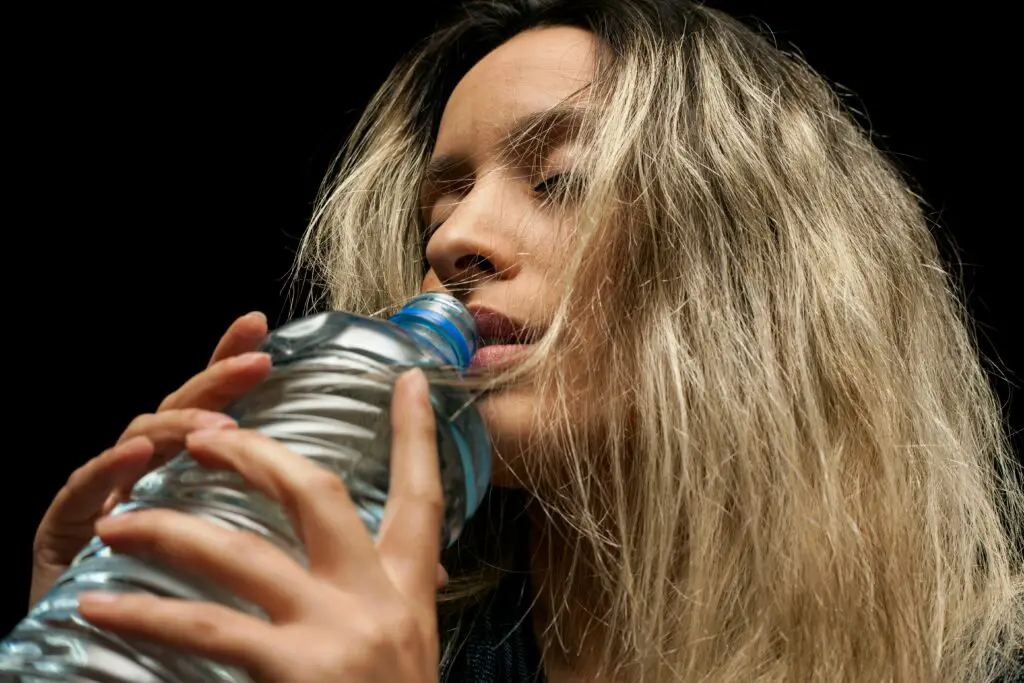 Close-up of a young woman with blond hair drinking from a plastic bottle.