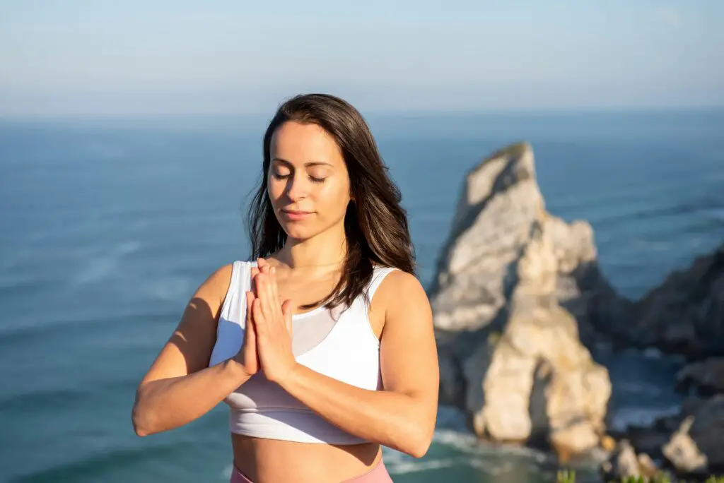 Woman meditating yoga outdoors by the ocean in Portugal, promoting relaxation and mindfulness.