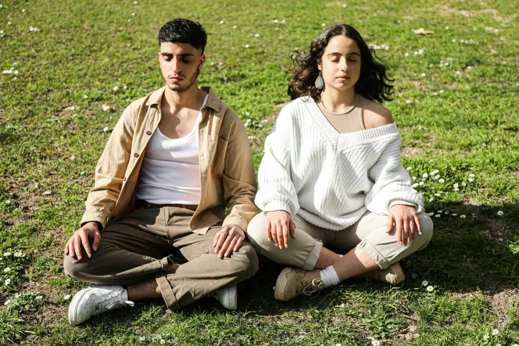 Man and woman doing deep breathing  outdoors with closed eyes on a sunny day, enhancing mindfulness and relaxation.