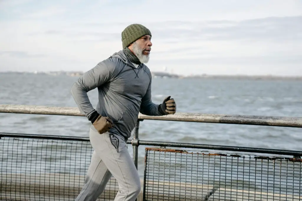 Elderly man jogging on promenade by the sea on a winter morning, showcasing active lifestyle.