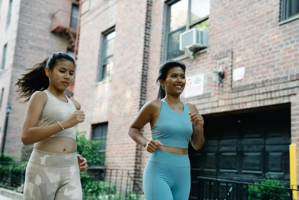 Two women jogging outdoors in sportswear through a city for fitness and healthy lifestyle.