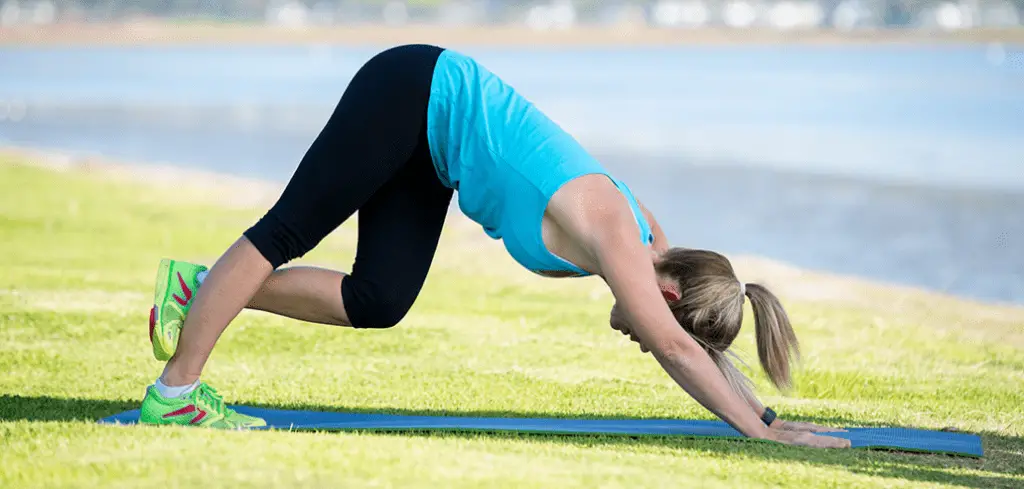 Woman doing stretching to prevent injuries in green grass .