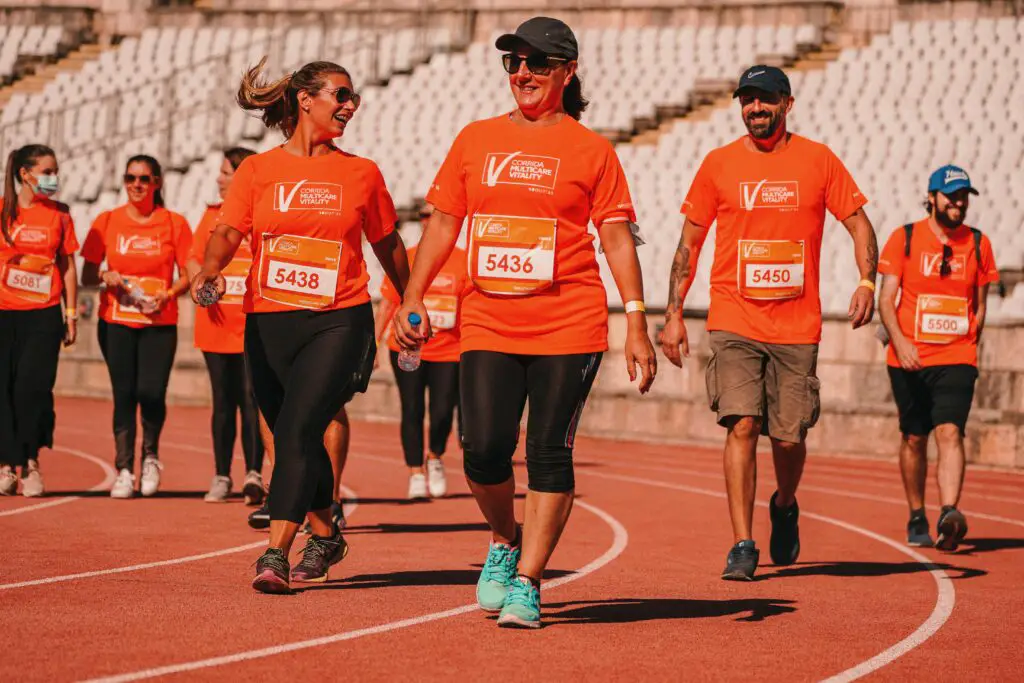 Group of people in bright orange shirts enjoying a walkathon on an outdoor track.