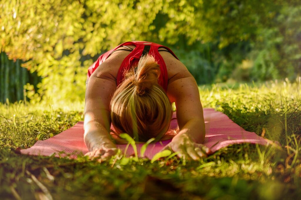 Person doing a static stretch on a yoga mat outdoors, demonstrating relaxation and flexibility in nature.