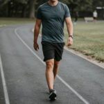 Low-intensity walking recovery for CrossFit athlete, relaxed stride on quiet track, breathable workout gear